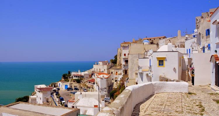 Petite ville côtière perchée sur les falaises, aux maisons blanches et pastel surplombant une mer cobalt sous un ciel dégagé