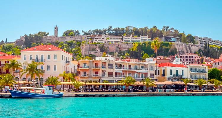 Colorful waterfront town with cafes and palm trees backed by a low fortress hill