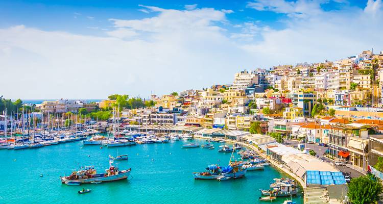 Bright harbour of Piraeus with turquoise water, fishing boats and terraced houses under a clear sky.