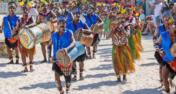 Lively beach parade of traditionally dressed islanders playing drums and dancing in bright costumes.