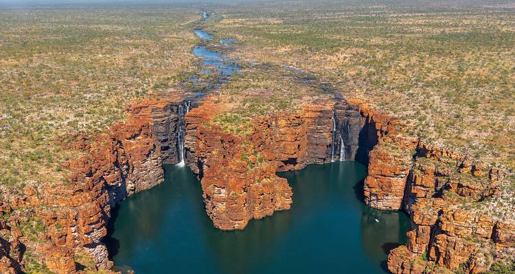 Aerial panorama of dramatic red sandstone gorge with twin waterfalls plunging into a deep blue river pool.