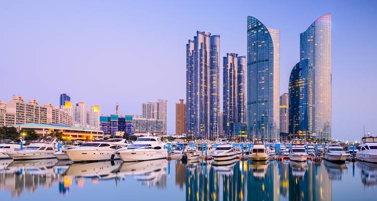 Sleek glass skyscrapers overlook a marina filled with yachts, all reflecting perfectly on calm dusk waters in a modern coastal city.