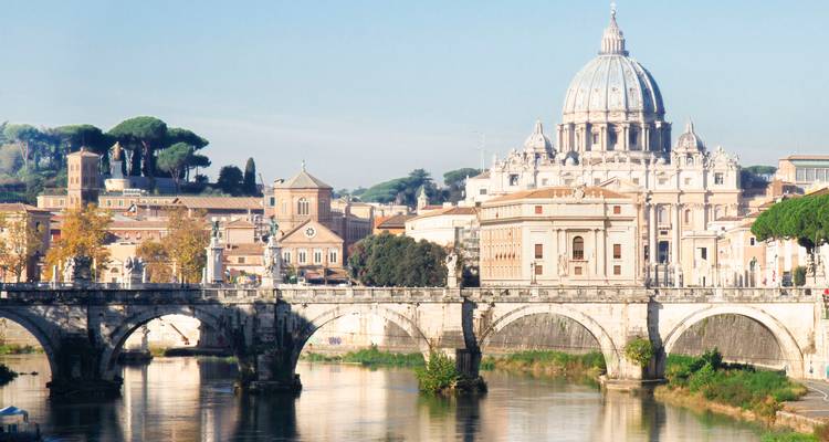 Vue classique de la Basilique Saint-Pierre et du Pont Sant'Angelo enjambant le Tibre à Rome sous un ciel bleu dégagé.