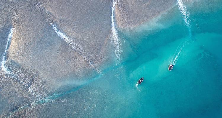 Aerial view of turquoise ocean channels and two small speedboats cutting white wakes through the water.