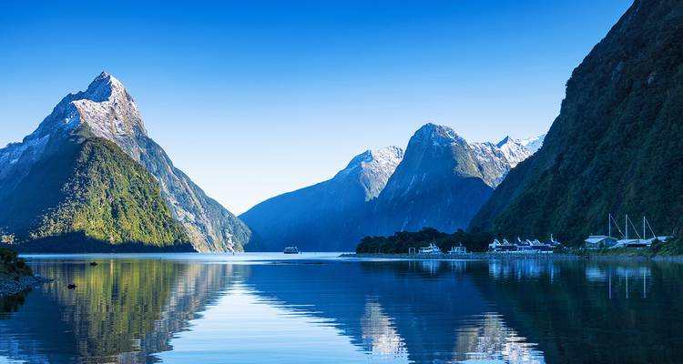Iconic Milford Sound fjord with steep snow-tipped peaks mirrored in calm blue water.