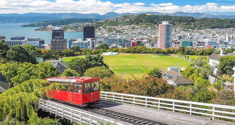 Bright red Wellington cable car overlooking city skyline, harbor, and green hills.