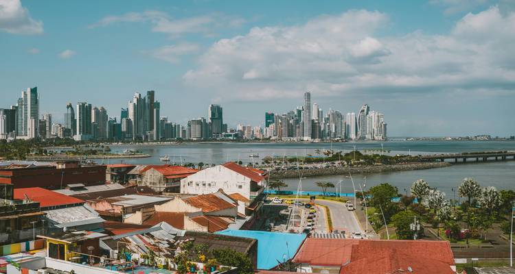 Wide view of Panama City skyline across the bay with colorful rooftops in foreground.