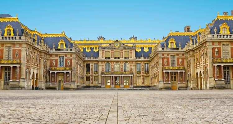 Vue de face symétrique du somptueux Palais de Versailles aux dorures ornementales sous un ciel bleu dégagé.