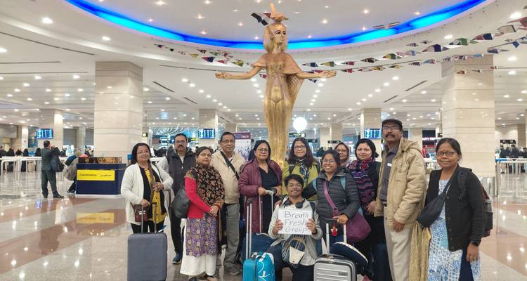 Un grand groupe de touristes avec bagages se rassemble pour une photo dans un hall d'aéroport brillamment éclairé sous une statue ailée dorée.