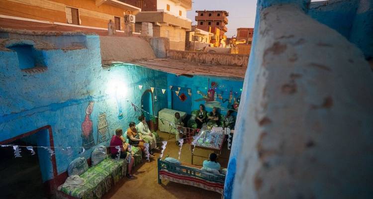 Rassemblement en soirée à l'intérieur d'une maison nubienne aux couleurs vives, avec des invités conversant autour de tables basses.
