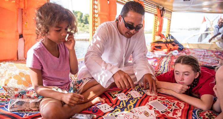 Guide and children playing cards on patterned cushions aboard a traditional felucca.