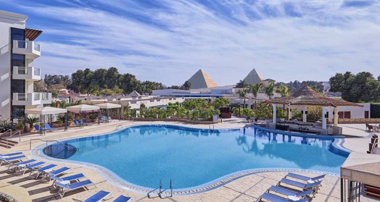 Resort swimming pool with sun loungers and a distant view of the Giza Pyramids.