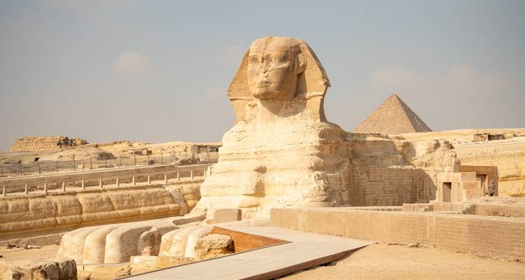 Iconic Sphinx fronted by a wooden walkway with a pyramid rising behind in the hazy desert light.