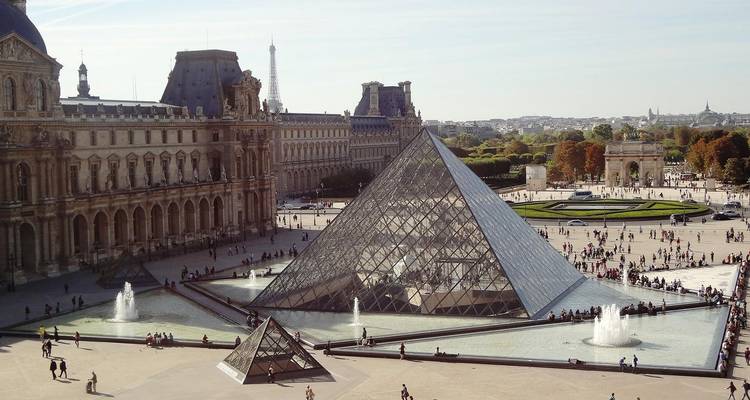 Aerial view of the Louvre courtyard with its glass pyramid, fountains and surrounding palace buildings.