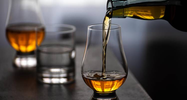 Close-up of golden whisky being poured into a tulip glass beside water glasses