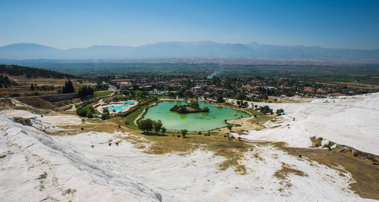 Breiter Blick von den weißen Travertinterrassen von Pamukkale über einen grünen Pool und entfernte Ebenen.
