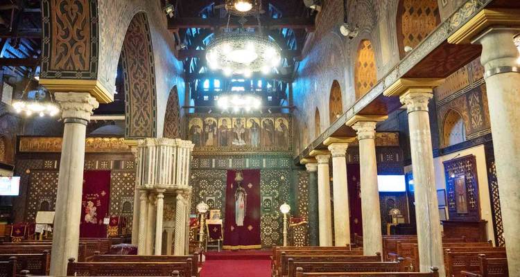 Richly decorated interior of Cairo’s Hanging Church featuring wooden ceiling beams, striped columns and glowing chandeliers.