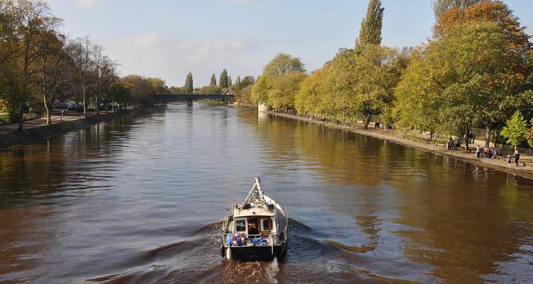 Eine kleine Bootsfahrt auf dem ruhigen Fluss Ouse, der in York von Herbstbaeumen gesaeumt ist