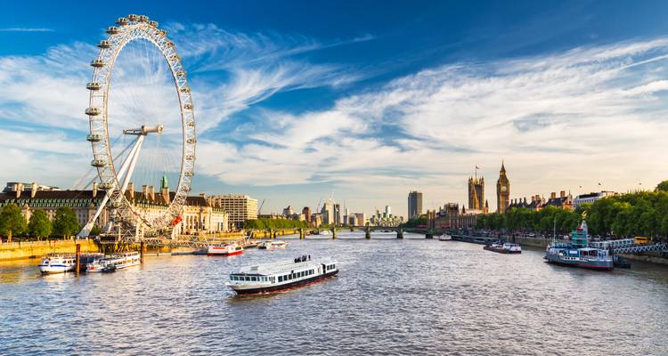 Weitblick auf die Themse mit Ausflugsbooten, die am London Eye und dem Palace of Westminster unter einem strahlend blauen Himmel vorbeifahren.