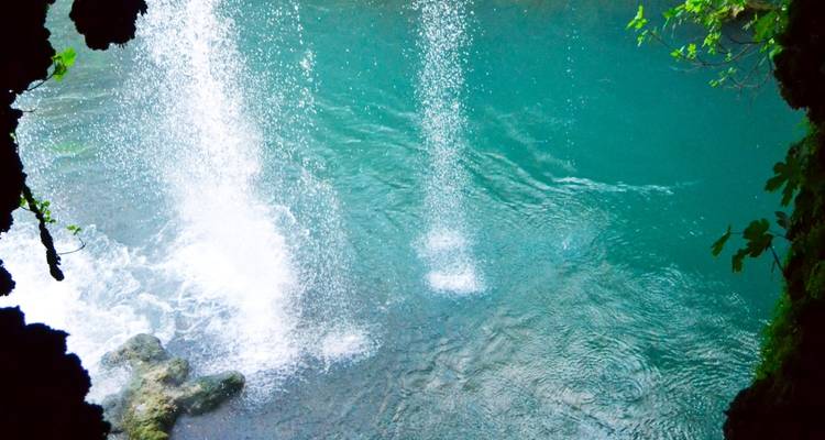 Les jets d'eau cascadent d'une falaise dans un bassin turquoise cristallin situé à l'intérieur d'une grotte rocheuse.