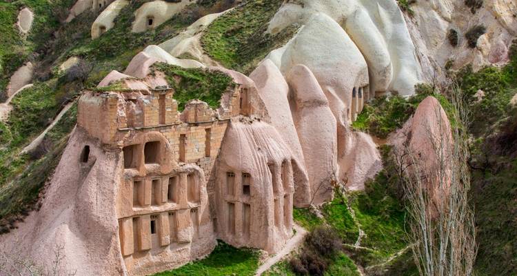 Rosa und helle Formationen Kappadokiens, übersät mit antiken Höhlenwohnungen inmitten grüner Hänge.