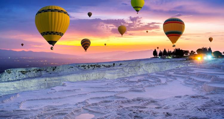 Der Abendhimmel leuchtet über den Terrassen von Pamukkale, während farbenfrohe Ballone über den Kalziumbecken aufsteigen.