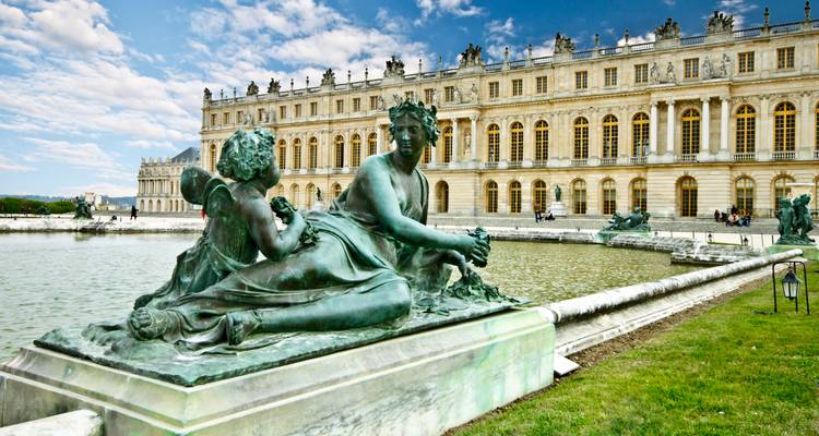 Elegant bronze statues beside the vast façade of the Palace of Versailles and its reflecting pool.