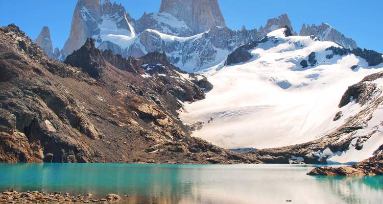 Schneebedeckte Türme des Mount Fitz Roy spiegeln sich in einer klaren türkisfarbenen Lagune wider, die von felsiger Moräne umgeben ist.