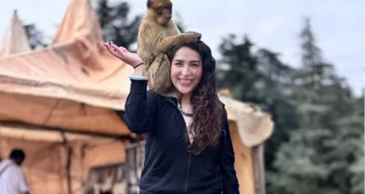 A woman smiles with a small monkey perched on her head at an outdoor market stall.