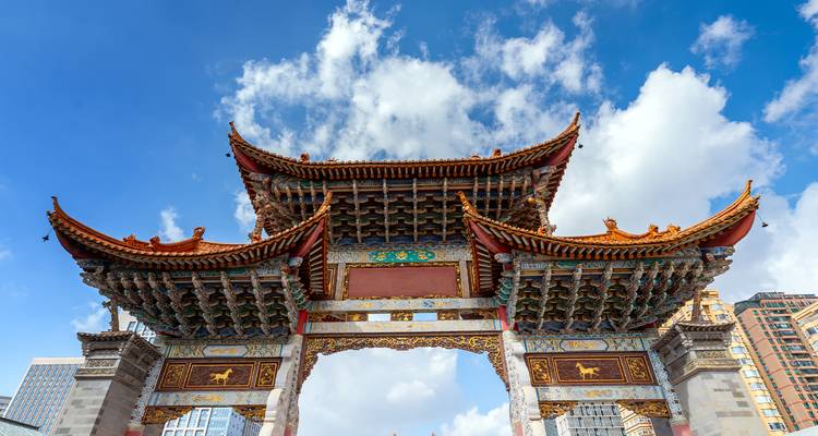 Decorative traditional Chinese archway against a bright blue sky and fluffy clouds.