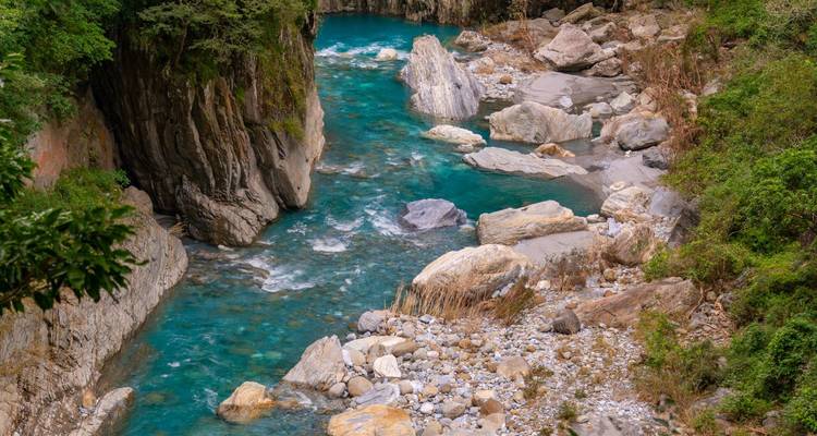 Turquoise river winding through steep rocky canyon with lush vegetation.
