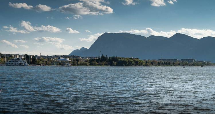 Expansive lake with distant city shoreline and mountain silhouette beneath a blue sky.