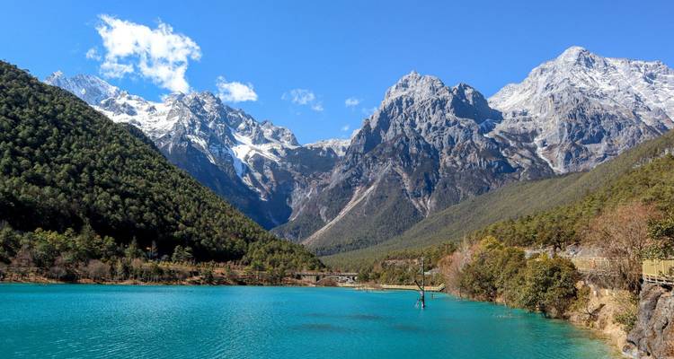 Crystal blue alpine lake framed by snowy peaks of Jade Dragon Snow Mountain under clear skies.