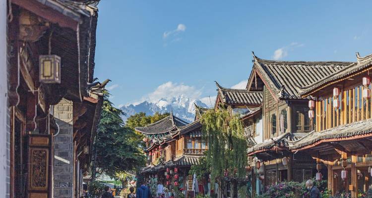 Bustling pedestrian street of Lijiang old town with snow-capped peaks visible in the distance.