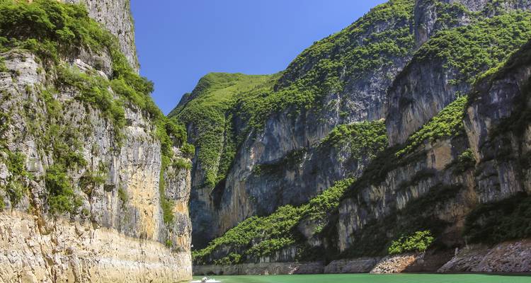 Steile Kalksteinklippen, die von Grün bewachsen sind und über den smaragdgrünen Wassern der Qutang-Schlucht an einem sonnigen Tag aufragen