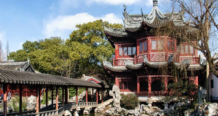 Traditioneller roter Pavillon und Zickzack-Brücke im klassischen Yu-Garten von Shanghai, umgeben von Grünflächen