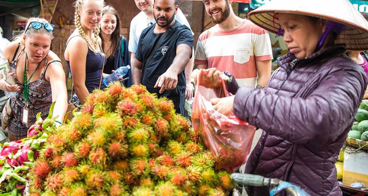 Travelers sample vibrant tropical fruit at a bustling Vietnamese market stall.