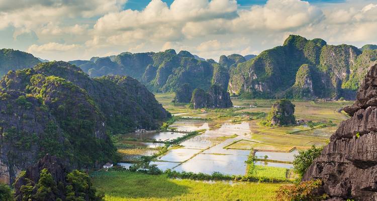 Sweeping view of lush limestone mountains, rice fields and reflective ponds in Ninh Binh countryside.