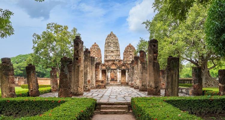 Ancient sandstone temple ruins surrounded by manicured green hedges at Sukhothai Historical Park.