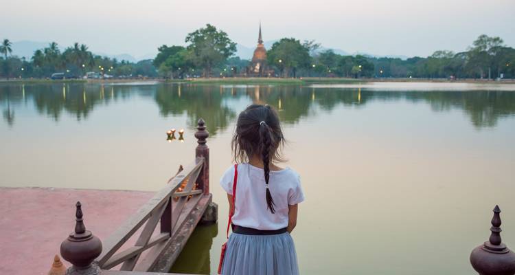 Young girl gazes across a tranquil lake at dusk toward a distant stupa in Sukhothai Park.