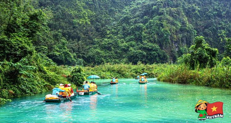 Multiple boats with life-jacketed travelers gliding along an emerald river in a limestone valley