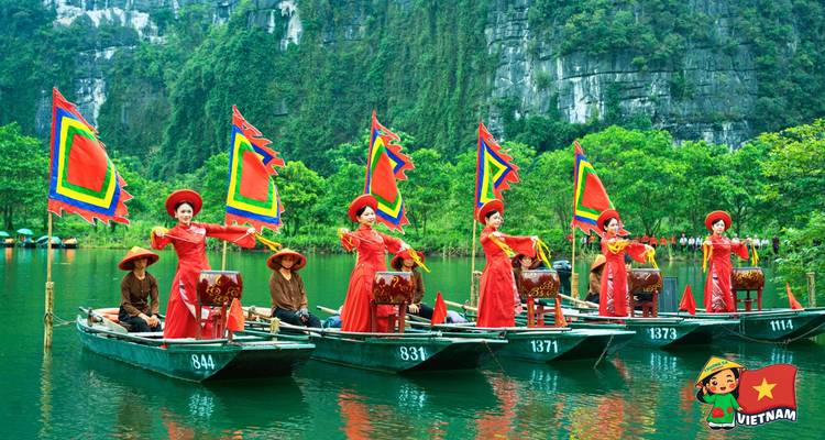 Performers in red traditional dresses standing on sampan boats with colorful flags on a green lake