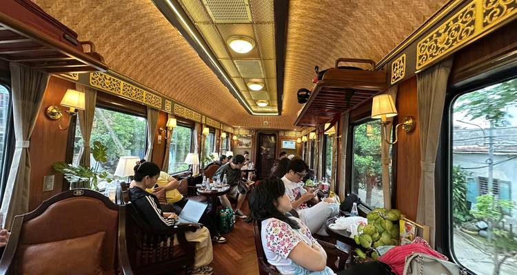 Spacious vintage train lounge with wood paneling where travelers relax at tables by large windows