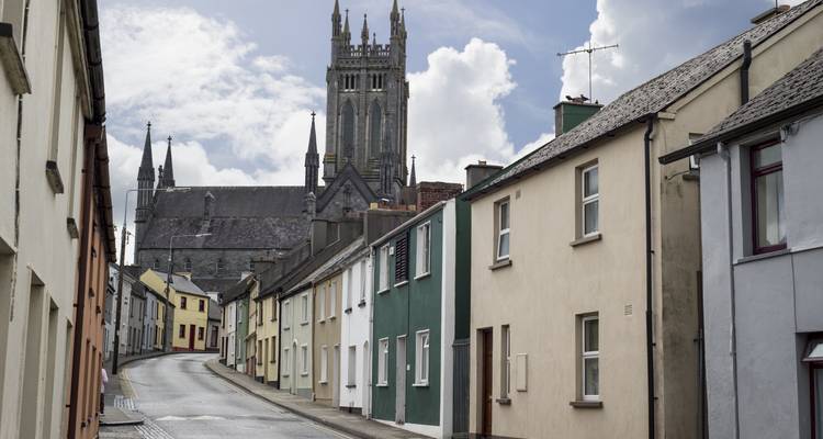 Row of pastel townhouses lining a narrow street with a gothic cathedral tower rising behind