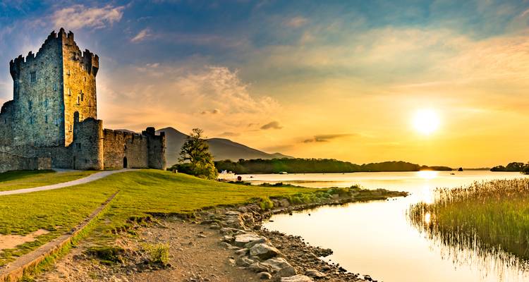 Medieval lakeside castle silhouetted against a dramatic sunset sky with calm reflective water