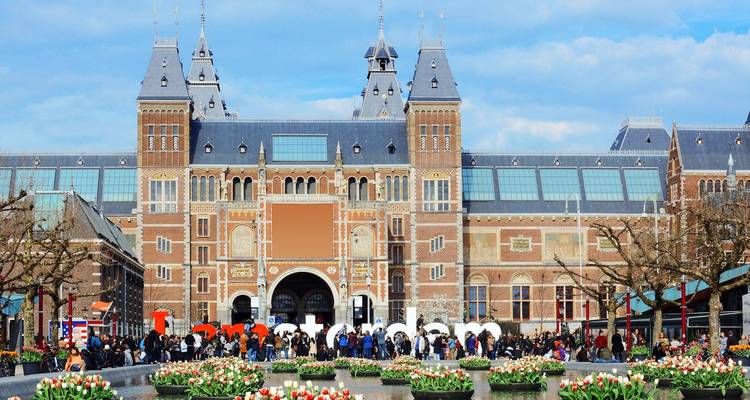 Front façade of Amsterdam’s Rijksmuseum with crowds and vibrant tulip beds in foreground.