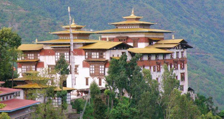 Un dzong perché au sommet d'une colline, aux murs blanchis à la chaux et aux toits dorés, domine une vallée verdoyante.