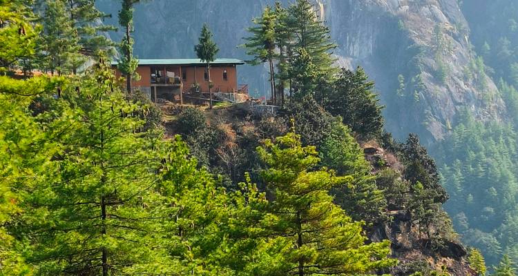 Une maison solitaire perchée sur une falaise couverte de pins dans les contreforts de l'Himalaya.