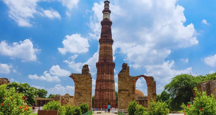 Der hohe Sandstein-Qutub-Minar-Turm erhebt sich über antike Ruinen unter einem strahlend blauen Himmel