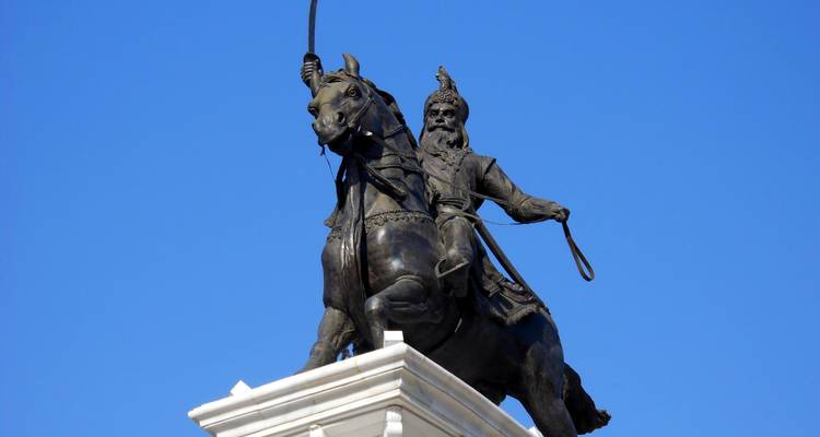Bronze equestrian statue of a Sikh leader poised against a deep blue sky.
